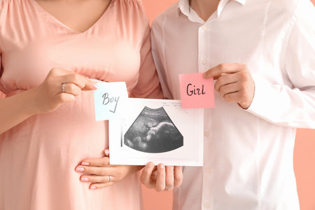 Young pregnant couple holding sonogram image and papers with sex of baby on pink background, closeupの写真素材