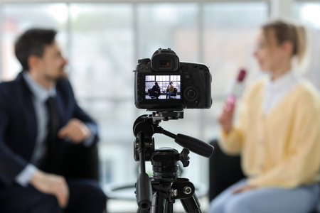 Female journalist with microphone having an interview with man on camera screen in office, closeupの写真素材