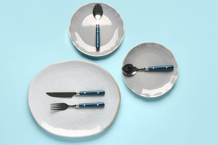 Table setting with clean plates and cutlery on blue background