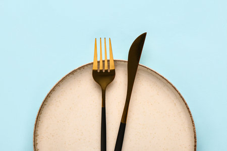 Table setting with clean plate and cutlery on blue background