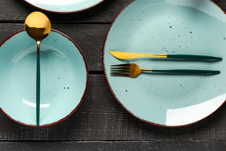 Table setting with clean plates and cutlery on black wooden tableの写真素材