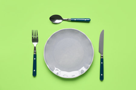 Table setting with clean plate and cutlery on green backgroundの写真素材