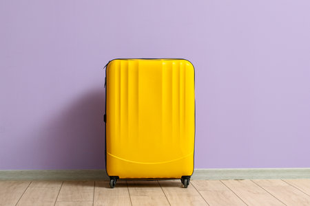 yellow suitcase near lilac wallの写真素材