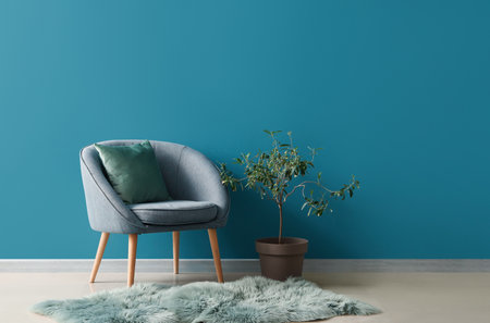 Cozy armchair with cushion, fur rug and houseplant on stool near blue wallの写真素材