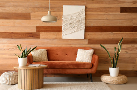Cozy brown sofa with cushions and houseplant on coffee table in living roomの写真素材