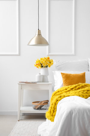Vase with beautiful narcissus flowers on bedside table in interior of bedroomの写真素材