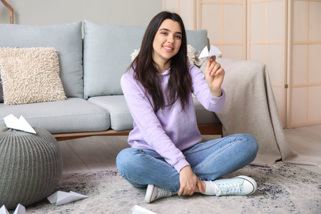 Young woman with paper plane sitting at homeの写真素材