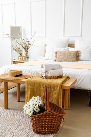 Interior of light bedroom with chrysanthemum flowers in basket and blooming tree branches on bedside tableの写真素材