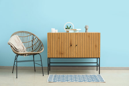 Stylish wooden cabinet and cozy armchair near blue wall