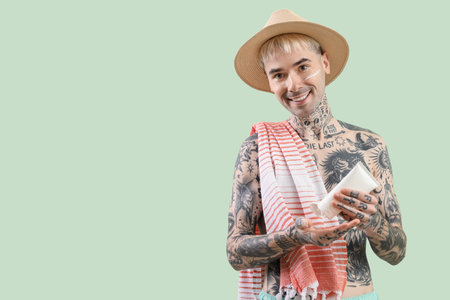 Tattooed man applying sunscreen cream on light green backgroundの写真素材