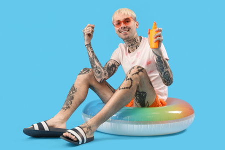 Tattooed man with sunscreen cream and swimming ring on light blue backgroundの写真素材