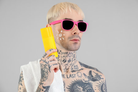 Tattooed man with sunscreen cream on light backgroundの写真素材