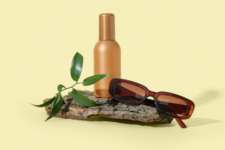 Bottle of sunscreen cream with sunglasses and tree bark on pale yellow backgroundの写真素材
