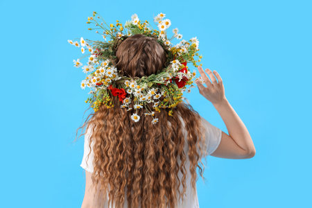 Beautiful young woman in flower wreath on blue background, back view. summer solsticeの写真素材