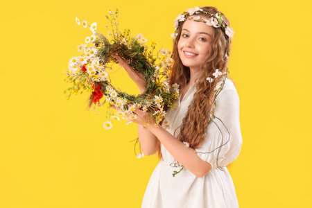 Beautiful young woman with flower wreath on yellow background. summer solsticeの写真素材