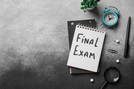 Notebooks with text FINAL EXAM, alarm clock and magnifier on grunge backgroundの写真素材