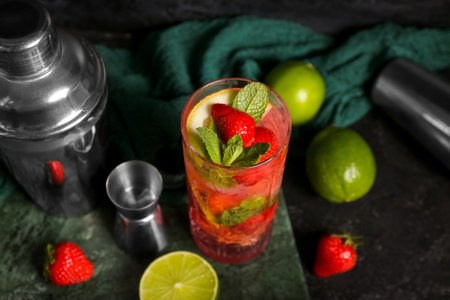 Stands with glasses of fresh strawberry mojito, jigger and shaker on black background