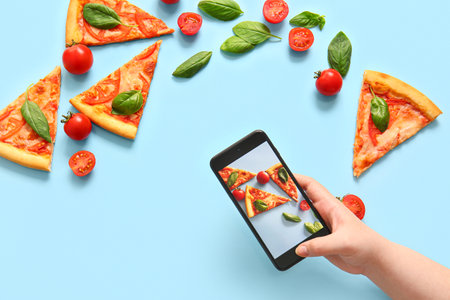 Woman taking photo of tasty pizza margarita on blue backgroundの写真素材