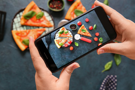 Woman taking photo of tasty pizza margarita on grunge black background
