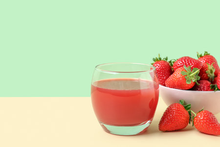 Glass of juice and bowl with strawberry on beige tableの写真素材