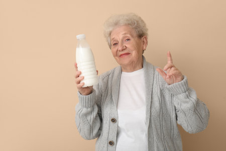 Senior woman with bottle of milk pointing at something on beige backgroundの写真素材