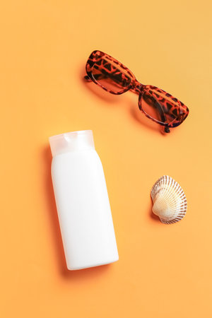 Bottle of sunscreen cream with sunglasses and seashell on orange backgroundの写真素材