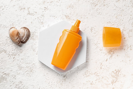 Stand with bottle of sunscreen cream and seashells on grunge white backgroundの写真素材