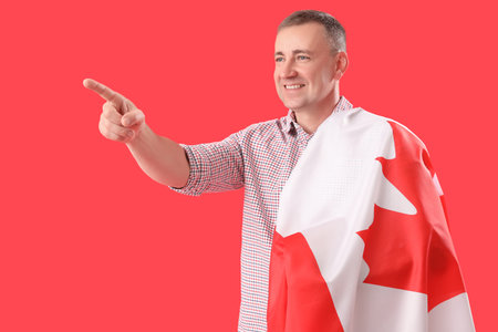 Mature man with flag of Canada pointing at something on red backgroundの写真素材