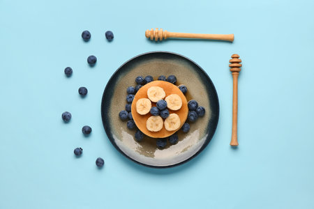 Plate with sweet pancakes, banana and blueberry on blue backgroundの写真素材