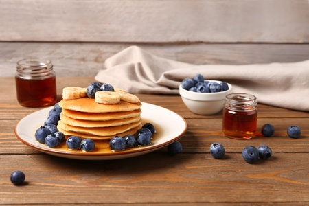 Plate with sweet pancakes, banana, blueberry and honey on wooden table, closeupの写真素材