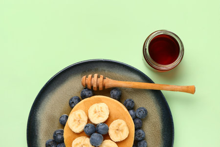 Plate with sweet pancakes, banana, blueberry and honey on green backgroundの写真素材