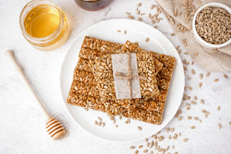 Plate with tasty kozinaki, sunflower seeds and jars of honey on white backgroundの写真素材