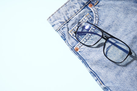 Stylish jeans with black eyeglasses on pale blue backgroundの写真素材