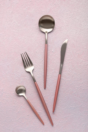 Stainless steel cutlery with pink handles on lilac background