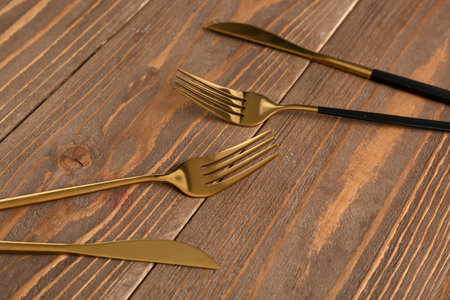 Golden forks and knives on wooden backgroundの写真素材