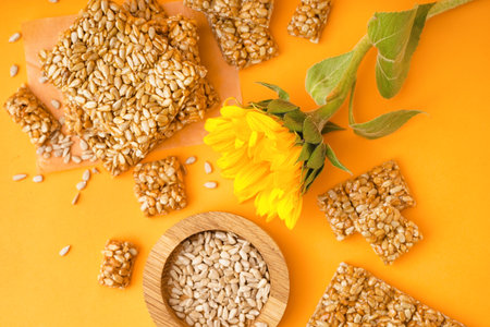 Wooden bowl of seeds with sunflower and tasty kozinaki on orange backgroundの写真素材