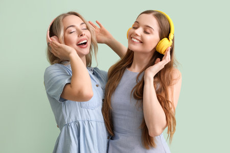 Young sisters in headphones on green backgroundの写真素材
