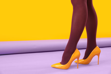 Female legs in black tights and yellow high heels on color backgroundの写真素材