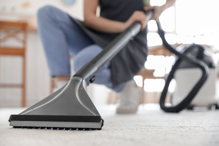 Young woman vacuuming carpet in kitchenの写真素材