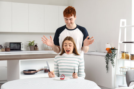 Young man proposing to his happy girlfriend in the kitchenの写真素材