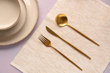 Plates with golden cutlery on lilac background