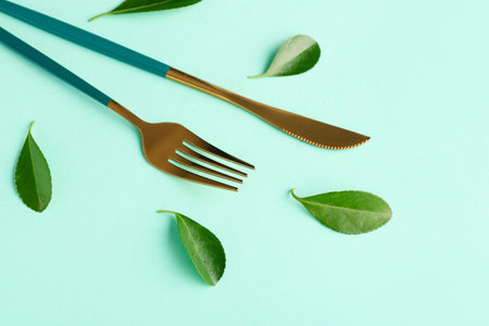 Stylish fork and knife with leaves on green background