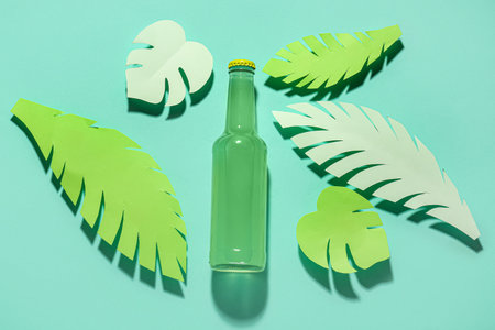 Composition with bottle of fresh soda and paper leaves on turquoise backgroundの写真素材