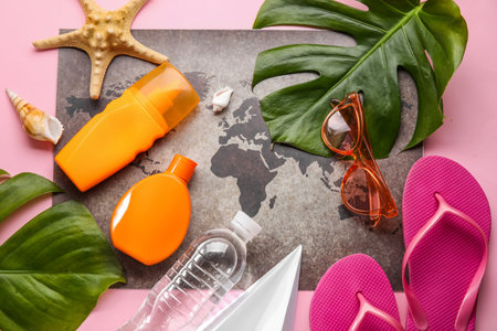 Composition with world map, bottles of sunscreen cream, tropical leaves and sunglasses on pink...