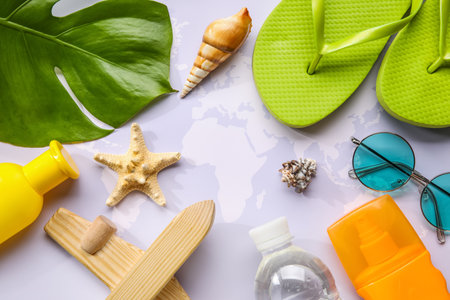 Composition with bottle of sunscreen cream, wooden plane, starfish and flip-flops on world mapの写真素材