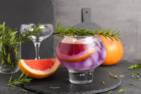 Glass of purple gin and tonic with rosemary and grapefruit on dark grunge table near wallの写真素材