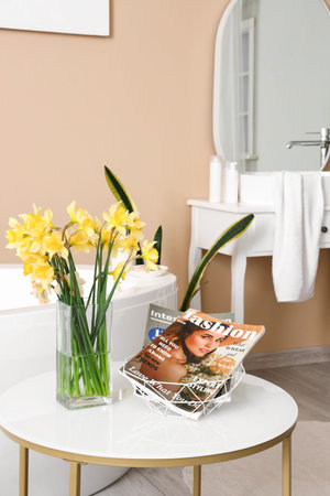 Vase with narcissus flowers and magazine on table in interior of bathroomの写真素材