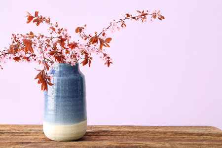Vase with blooming tree branches on wooden table against pink backgroundの写真素材