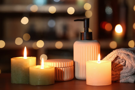 Burning candles, bath supplies and rolled towel on table against blurred lights, closeupの写真素材