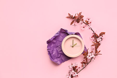 Blooming tree branches with flowers and alarm clock on pink backgroundの写真素材